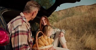 Gri saçlı bir adam yeşil kareli gömlekli mutlu karısıyla ve küçük kızıyla iletişim kuruyor. Onlar şehrin dışındaki pikniklerinde açık bir bagajda otururken sarışın bir kız.