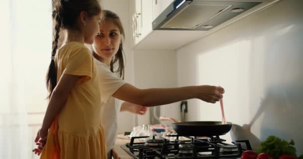 黄色いドレスの小さなブルネットの少女は 彼女がキッチンで朝食を用意しながら 母親と通信する — ストック動画