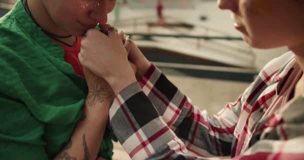在滑冰场附近的公园里 一个穿着绿色衬衫的女孩在亲吻她的女朋友们的手的特写镜头 同性恋夫妇在公园的约会中牵着手亲吻对方的手 — 图库视频影像