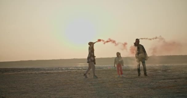 一个快乐的黑发女孩 身穿绿色格子衬衫 与丈夫和小女儿一起玩烟火 在荒芜的海面上散发出绿色和红色的烟雾 — 图库视频影像