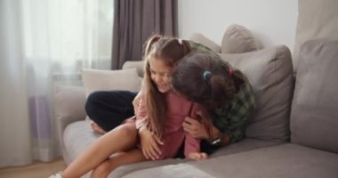 Mutlu baba, yeşil kareli gömlekli esmer bir adam pembe elbiseli esmer kızıyla oynuyor ve modern bir dairede gri bir koltukta otururken onu gıdıklıyor..