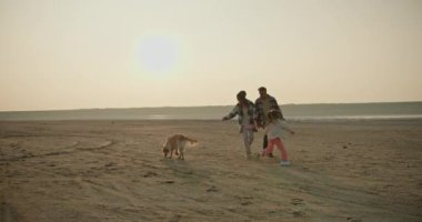 Mutlu aile, yaz akşamı dinlenirken evcil köpeğiyle şehir dışında oynuyor. Kareli tişörtlü, orta yaşlı esmer bir adam ve karısı ve küçük kızı büyük kızlarıyla oynuyorlar.