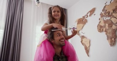 Sihirli değnekli, peri kostümlü esmer bir kız babasının omuzlarında oturur ve modern dairelerinde dolaşırlar..