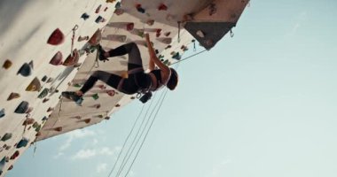 Alt manzara: atletik bir kız tırmanma duvarındaki gerekli yüksekliğe tırmanır ve güvenlik ağı kullanarak aşağı iner. Sarışın bir kız kaya tırmanışı dersinde ip kullanarak yere yığılıyor..