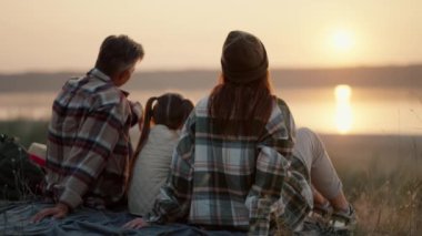 Mutlu bir aile eşinin ve küçük kızının şehir dışında tatil ve piknik yaparken mindere oturup yaz akşamları göletin yanındaki gün batımını izlediği arka manzara..