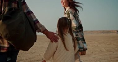 Mutlu bir ailenin arka görüntüsü, kareli tişörtlü orta yaşlı bir adam deniz kıyısında karısı, esmer bir kız ve beyaz ceketli küçük sarışın bir kızla birlikte yürür.