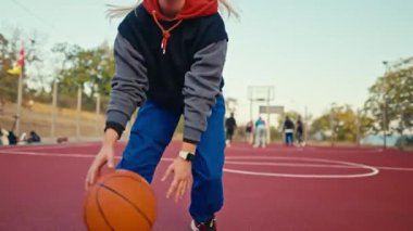 Spor üniformalı sarışın bir kızı kapat turuncu bir kılıçla koşar ve manevra yapar ve basketbol oynarken topu potaya atar..