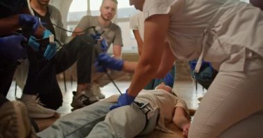Yakın çekim: Beyaz tıbbi üniformalı profesyonel bir hemşire-kız ilk yardım eğitimi sırasında bir kişinin bacağına tıbbi turnike uygulanması tekniğini gösteriyor.