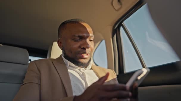 茶色のスーツの黒い肌の色の自信と幸せな男ビジネスマンは 携帯電話でさよならを言い 目的地を探して車の中で周りを見回します 黒肌の男性ビジネスマン — ストック動画