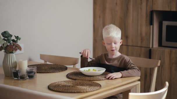 머리를 알비노 소년은 현대적인 부엌에서 의자에 앉아있는 식사를하는 오트밀을 먹습니다 — 비디오