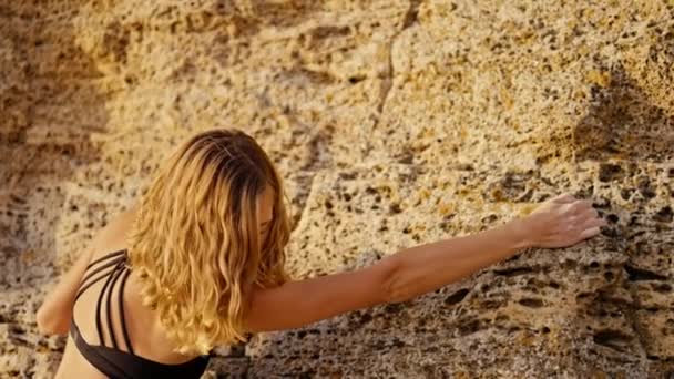 Blonde Girl Curly Hair Black Top Climbs Yellow Rock Looking — Stock Video