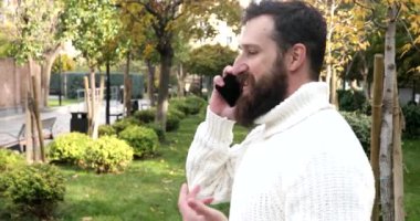 Yakışıklı, bakımlı ve sakallı bir genç adam. Açık havada akıllı telefon kullanıyor..