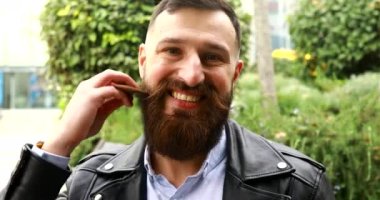 Sakallı genç adam dışarıda sakalını tarıyor..
