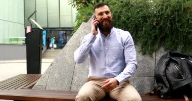 Yakışıklı, bakımlı ve sakallı bir genç adam. Açık havada akıllı telefon kullanıyor..