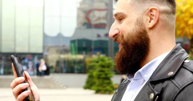 Yakışıklı, bakımlı ve sakallı bir genç adam. Açık havada akıllı telefon kullanıyor..