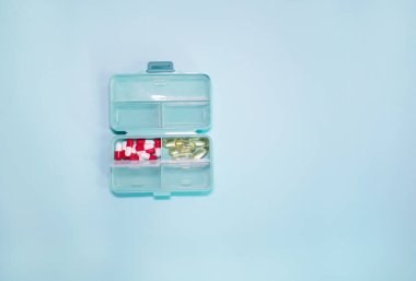 Açık mavi arka planda farklı haplar içeren plastik kutu.