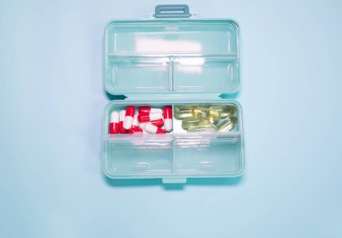 Açık mavi arka planda farklı haplar içeren plastik kutu.