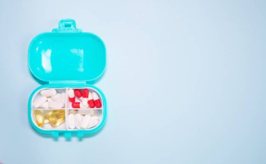 Açık mavi arka planda farklı haplar içeren plastik kutu.