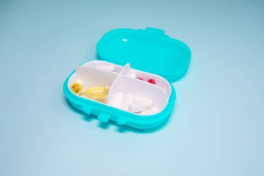 Açık mavi arka planda farklı haplar içeren plastik kutu.
