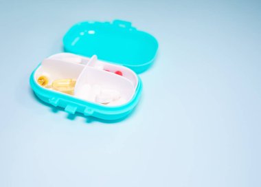 Açık mavi arka planda farklı haplar içeren plastik kutu.