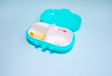 Açık mavi arka planda farklı haplar içeren plastik kutu.