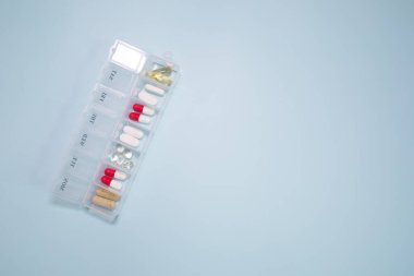 Açık mavi arka planda farklı haplar içeren plastik kutu.