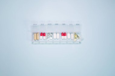 Açık mavi arka planda farklı haplar içeren plastik kutu.