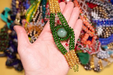 Close-up view of person holding jewelry, beads necklaces on yellow background