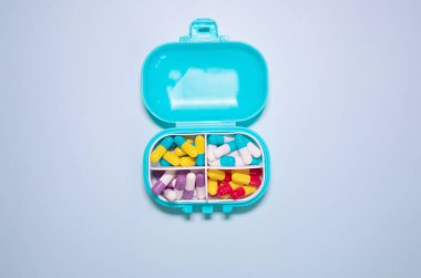 Plastic box with different pills on light blue background. Space for text