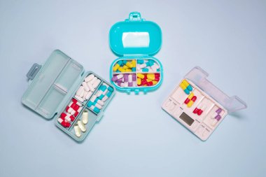 Plastic boxes with different pills on light blue background, top view. Space for text