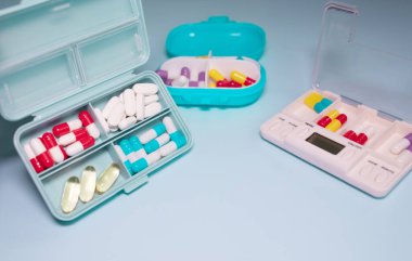 Plastic boxes with different pills on light blue background, top view. Space for text