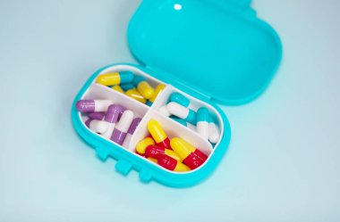 Plastic box with different pills on light blue background. Space for text