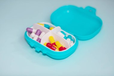 Plastic box with different pills on light blue background. Space for text