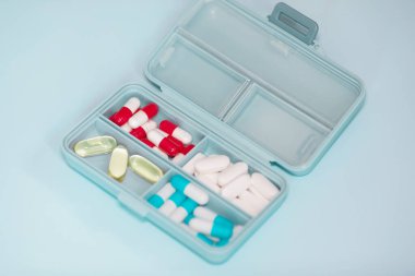 Plastic box with different pills on light blue background. Space for text