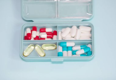 Plastic box with different pills on light blue background. Space for text