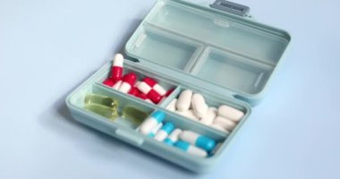 Plastic box with different pills on light blue background. Space for text