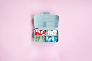 Plastic box with different pills on light pink background. Space for text