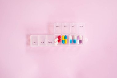 Plastic box with different pills on light pink background. Space for text