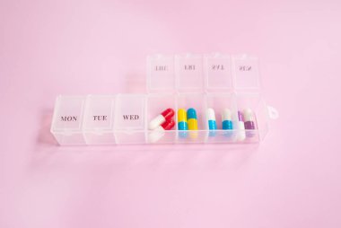 Açık pembe arka planda farklı haplar içeren plastik kutu. Metin için boşluk