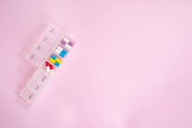 Açık pembe arka planda farklı haplar içeren plastik kutu. Metin için boşluk