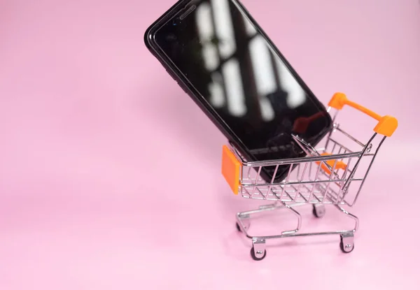 stock image shopping cart with smartphone on pink background