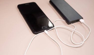 Powerbank bej arka planda akıllı telefonu şarj ediyor.