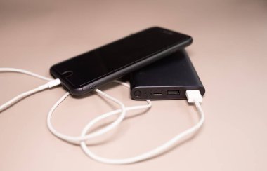 Powerbank bej arka planda akıllı telefonu şarj ediyor.