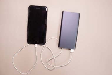 Powerbank bej arka planda akıllı telefonu şarj ediyor.