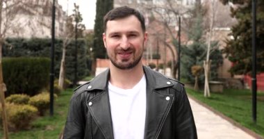Genç sakallı adam dışarıda gülümsüyor..