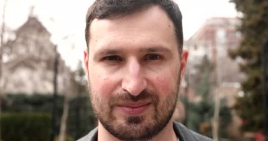 Genç sakallı adam dışarıda gülümsüyor..