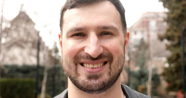 Stock image portrait of handsome bearded young man smiling at camera on street 