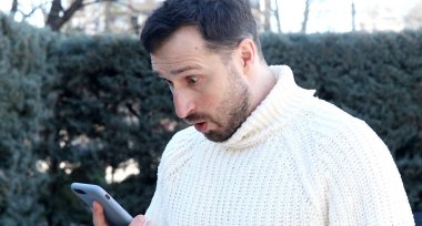 Heyecanlı genç adam akıllı telefon kullanıyor ve sokaklarda zaferi kutluyor 