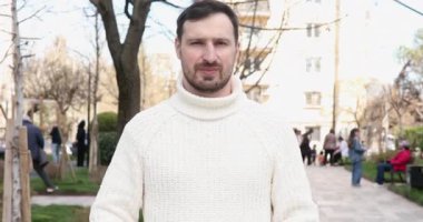 Yakışıklı, mutlu genç bir adam elleriyle bir şey sunuyor ve baş parmağını açık havada gösteriyor.