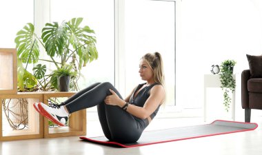 Spor kıyafetli zayıf bir sporcu kadın evde egzersiz yapmadan önce ısınma kaslarını çalıştırıyor..